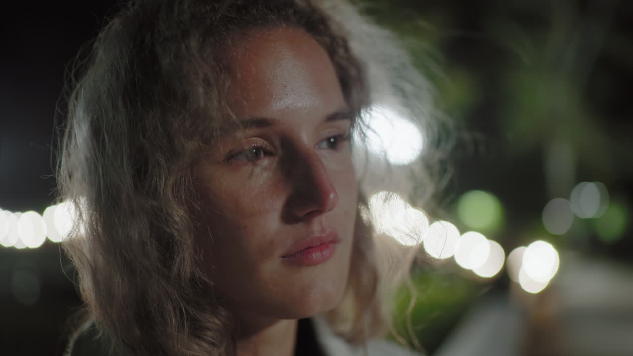 Close up white lady in deep thought, hair swaying in gentle night breeze, bokeh lights softly illuminating background, reflecting calm introspective mood