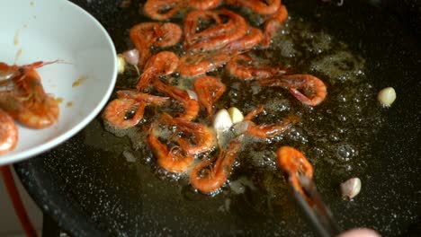 cook removing fried prawns from the heat and putting them on a plate during the preparation of fideua