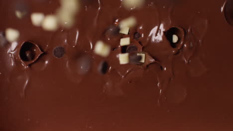 close up overhead shot of pieces of chocolate being dropped into melted chocolate sauce