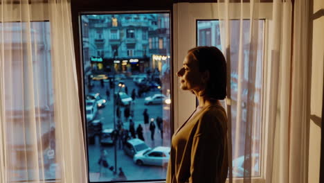 woman gazing out a window at a bustling city street at dusk