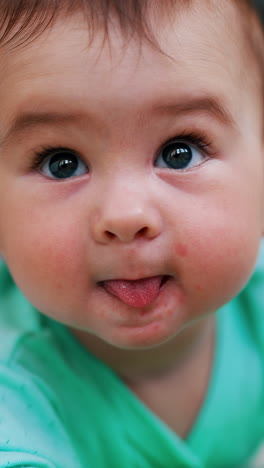 dear baby boy wearing blue clothes lies on belly. portrait of a nice active child showing tongue. close up. vertical video
