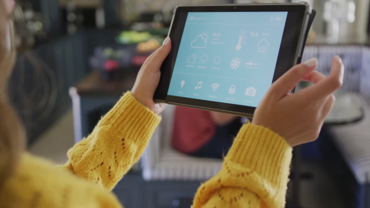 mujer biracial que pasa tiempo en casa usando una tableta con interfaz de hogar inteligente