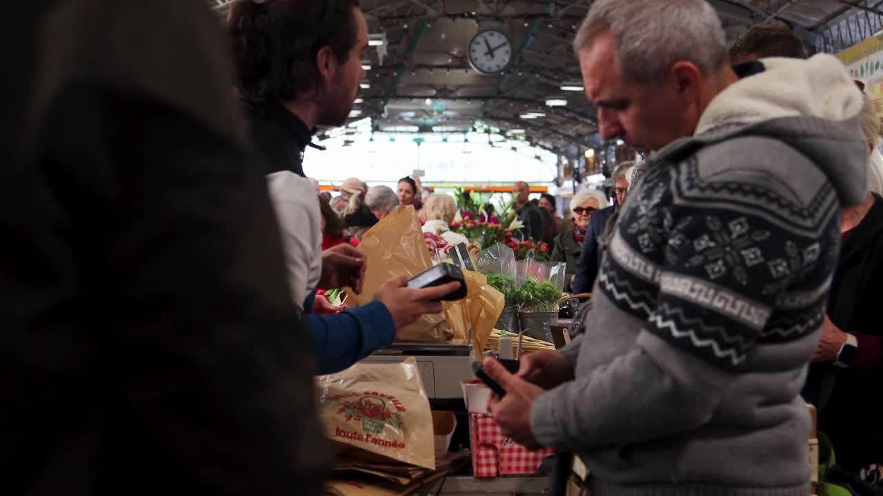 Man shopping at bustling indoor market in Antibes, receiving items in paper bag, casual atmosphere