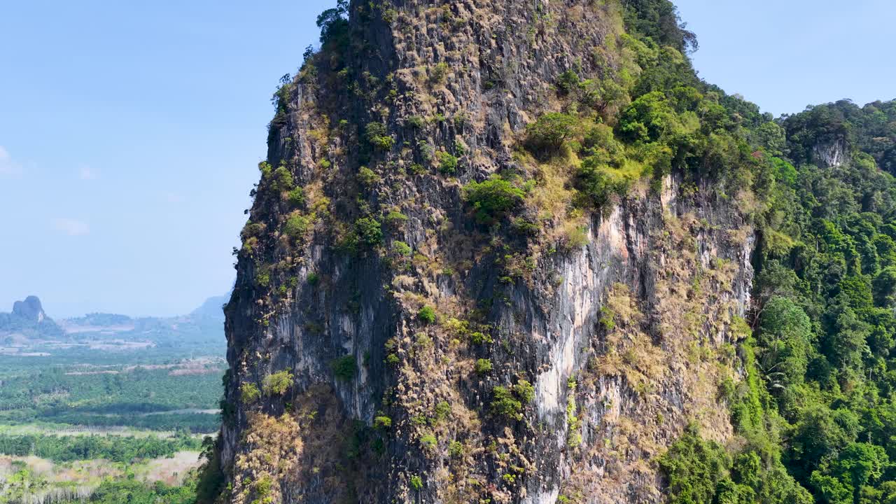 Rekaman drone mengorbit gunung karst batu kapur terjal yang menghadap pemandangan perkebunan kelapa sawit tropis