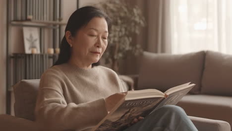 woman reading a book and drinking from a mug at home
