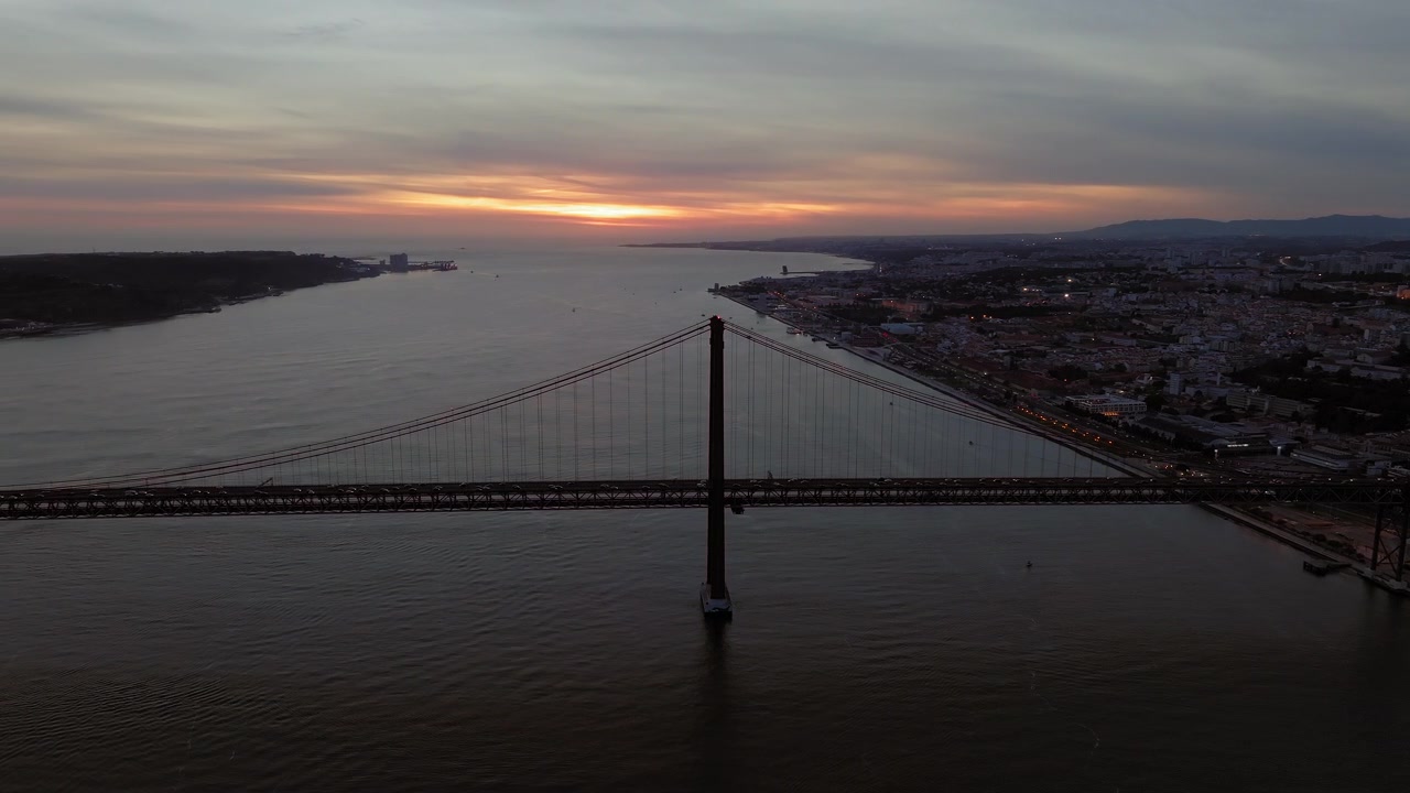 Drone in orbita intorno al Ponte 25 de Abril, al crepuscolo, con la luce dell'ora blu che si riflette sul fiume Tago, ripresa aerea. Lisbona, Portogallo