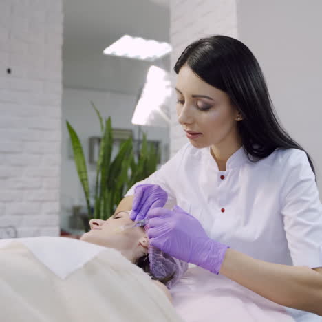 a beautician with long hair checks an injection and starts the biorevitalization procedure on the woman's face. blurred background.