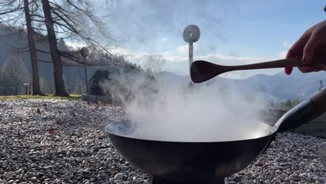 cooking in a wok over an open fire, stirring food