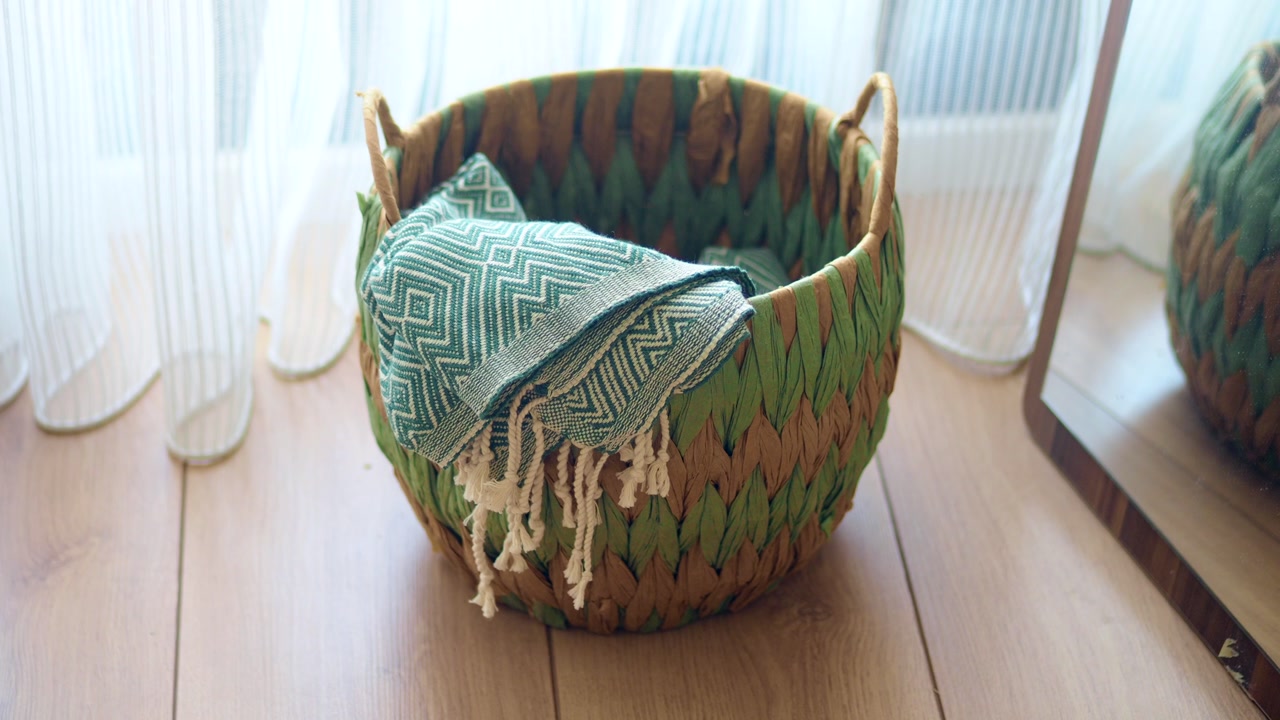 Green Woven Basket with Patterned Towel on Wooden Floor