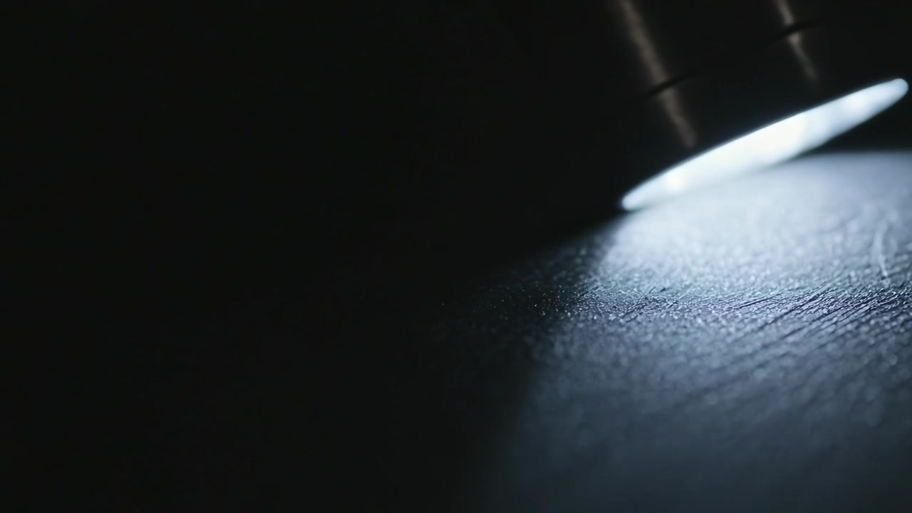 Switching on metal flashlight in dark space, beam tilting, revealing scuffed leather, copy space
