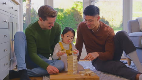 Familia-Con-Dos-Padres-Jugando-Con-Su-Hija-En-Casa-Apilando-Ladrillos-De-Madera-En-La-Torre