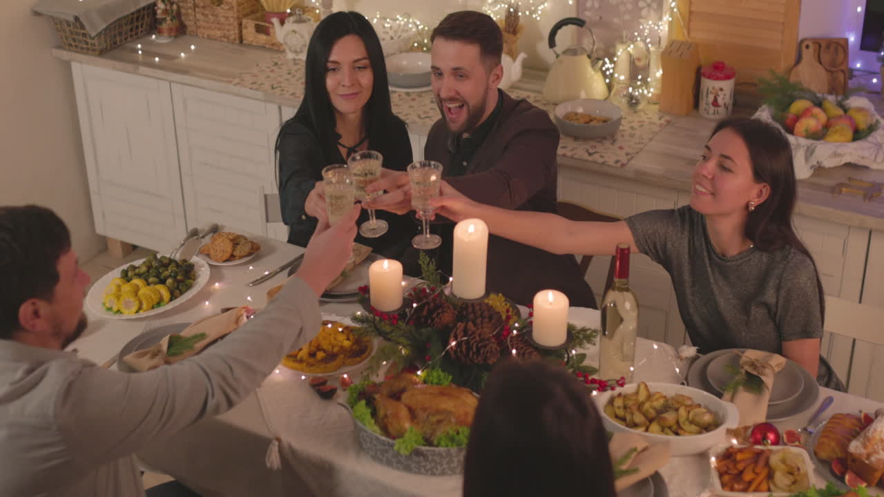 Gruppo di amici felici seduti a tavola che fanno un brindisi prima di cenare a Natale a casa.