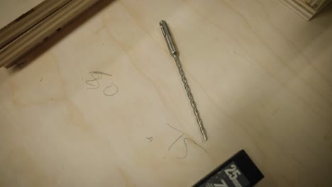 long drill bit and numbers written on wooden work bench