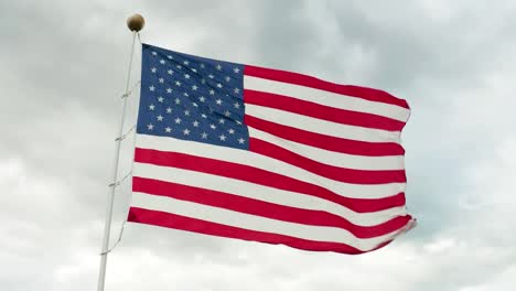 Aerial-of-American-flag-waving-in-wind-against-gray-storm-clouds-in-sky