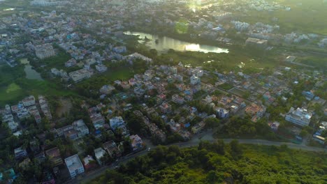 Drone-shot-of-a-city-showing-roads,-houses,-waterbodies-and-a-mountain-with-backwards-movement-and-upward-panning