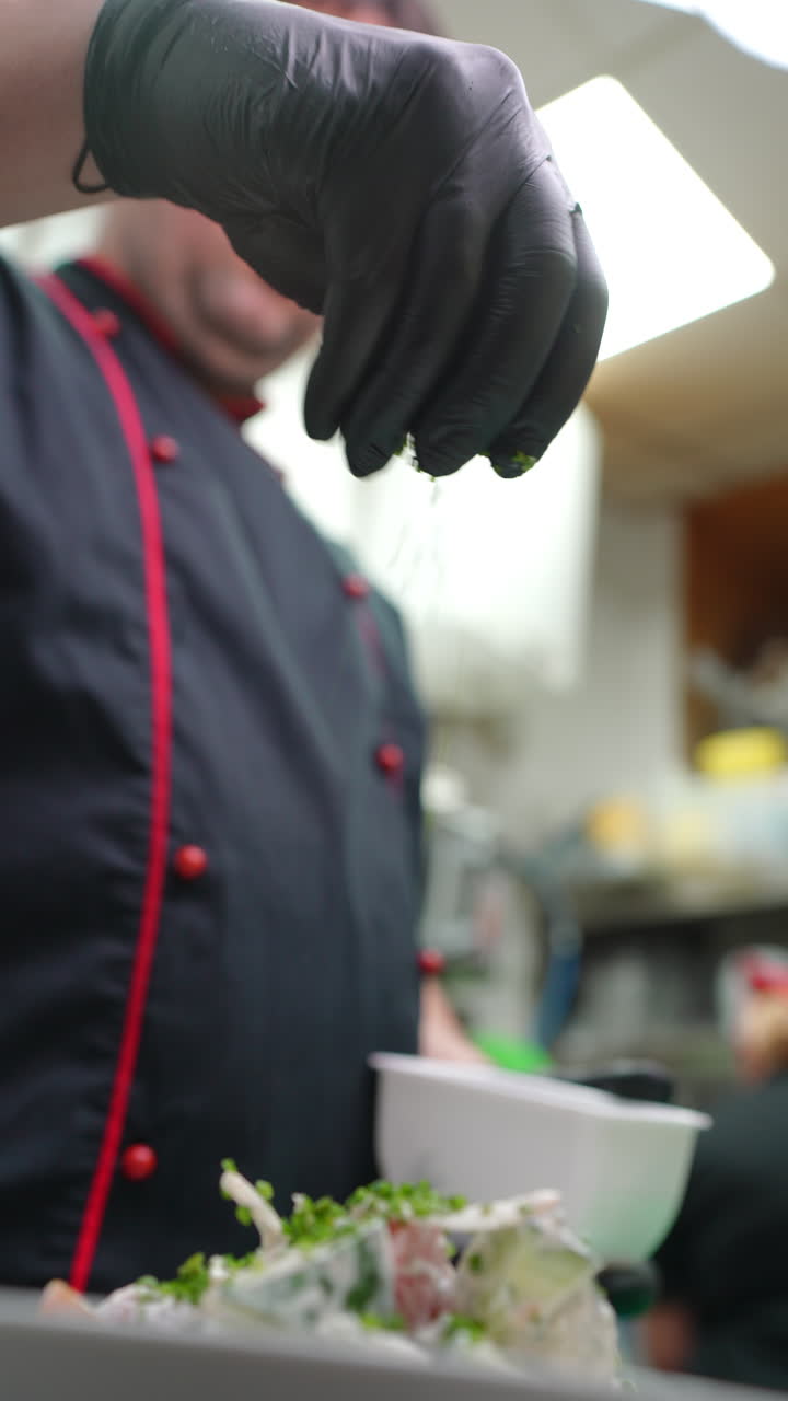 Vertical footage Professional chef in black food safe gloves carefully sprinkling freshly chopped chives over gourmet salad while working at restaurant kitchen counter