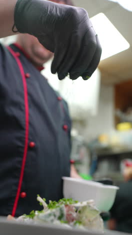 vertical footage professional chef in black food safe gloves carefully sprinkling freshly chopped chives over gourmet salad while working at restaurant kitchen counter
