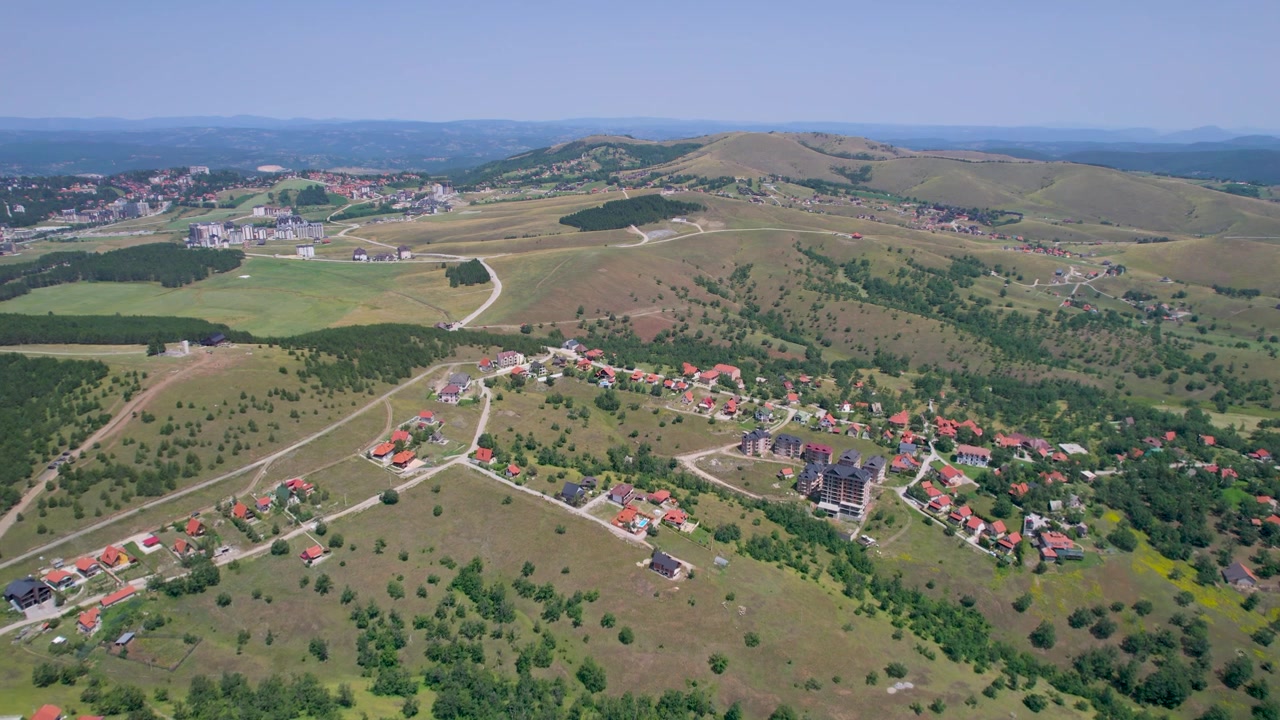 Een hoog dronebeeld overziet een landelijk dorp, vertakkende wegen, velden, bosgebied en glooiende heuvels die zich uitstrekken tot aan de horizon in Zlatibor, Servië.