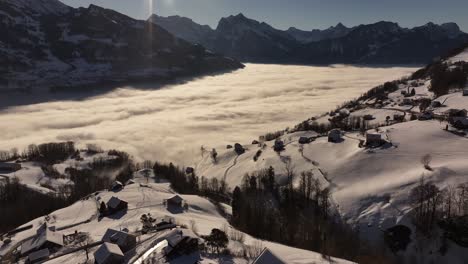 Breathtaking aerial view of Amden, Arvenbüel, Weesen and Glarus in Switzerland, drone glides forward toward thick cloud layer above lake as majestic Swiss alps rise above mist