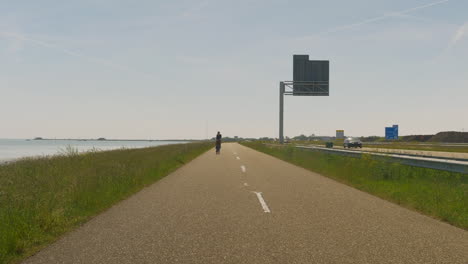 cyclist on a bike track adjacent to a motorway riding towards us