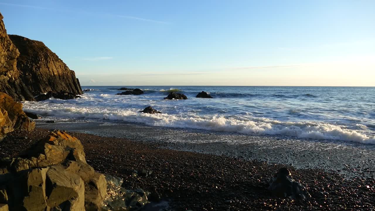 Irische Küste, goldene Stunde, weiße Brandung am Kiesstrand, keine Menschen, Copper Coast Waterford Irland, epische Landschaften