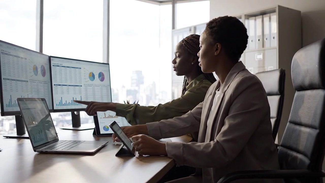 Professionals Collaborating in a Modern Office, Analyzing Data and Charts on Multiple Screens While Engaging in Productive Discussions about Business Insights