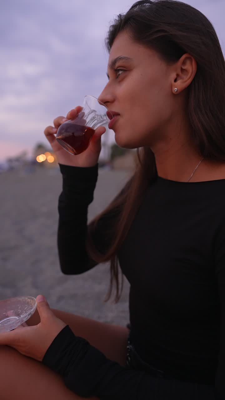 Young woman enjoying Turkish tea on the beach at sunset