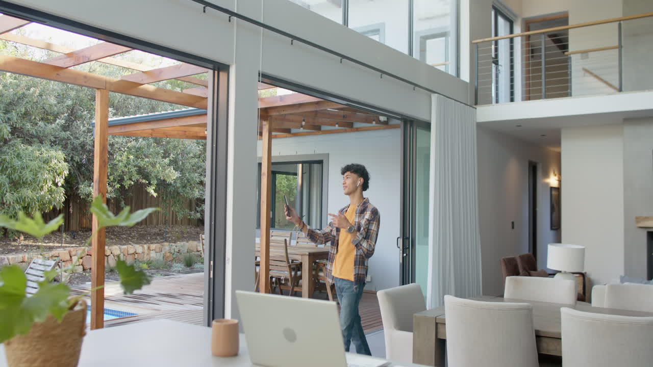 Opening sliding glass door, teenage boy enjoying fresh air in modern home with laptop