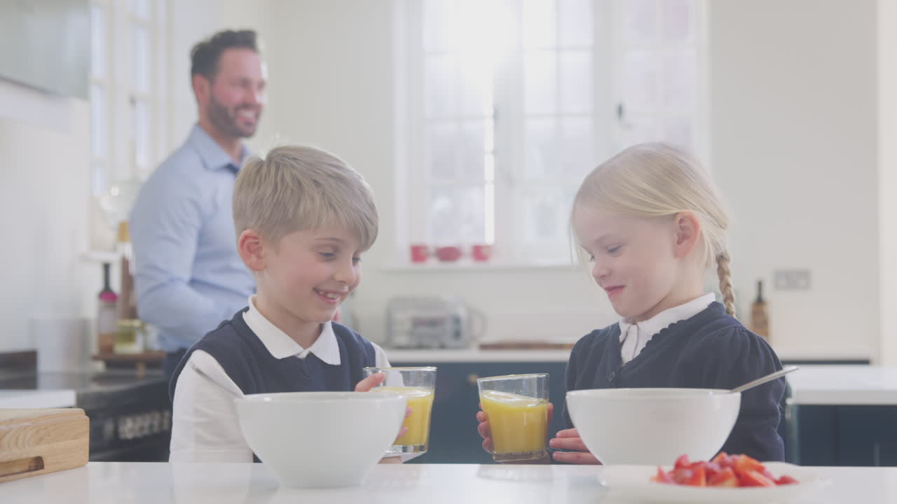 Due bambini che indossano l'uniforme scolastica in cucina a fare colazione mentre il padre si prepara per il lavoro