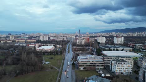 Panoramic-aerial-view-of-skyline-buildings,-road-through-cityscape-under-sunset-and-cloudy-sky,-Sofia,-Bulgaria