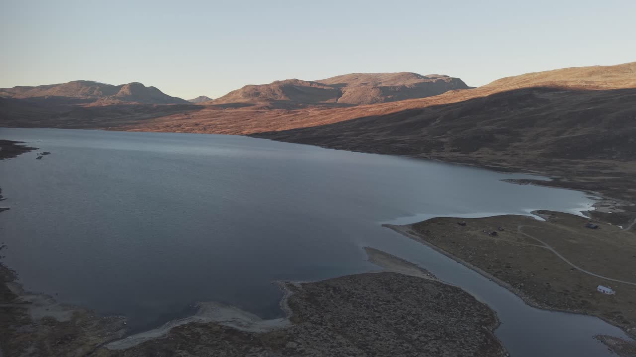 Panoramic view of mountain lake, surrounding mountains and a road along the lake. Drone footage, Norway