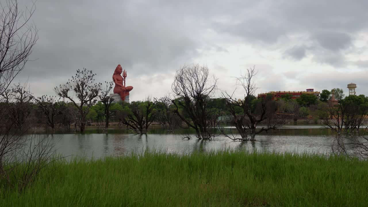 cloud movement timelapse over Meditating Shiva Statue with pristine lake and bright sky at Sunrise