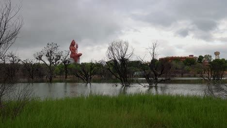 cloud movement timelapse over meditating shiva statue with pristine lake and bright sky at sunrise