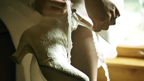 Close-up-view-of-young-bride-tying-her-white-shoelaces-on-white-shoes-while-getting-ready-for-her-wedding