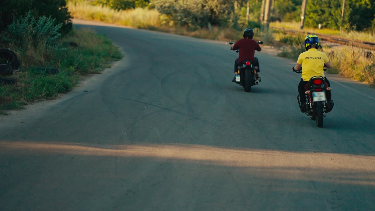 un instructor con una camiseta amarilla, junto con su estudiante de conducción de motocicleta, están girando en la esquina de la carretera. enseñando a montar una motocicleta