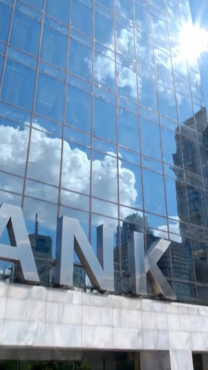 Uma Estrutura Bancária Contemporânea Exibindo Arquitetura Moderna e Reflexos Urbanos Sob um Céu Azul com Belos Padrões de Nuvens na Paisagem Urbana