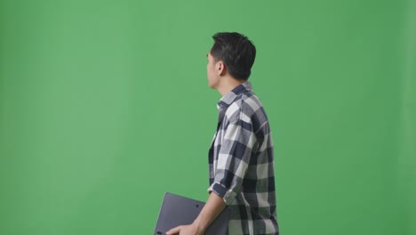 스튜디오에서 녹색 스크린에서 는 동안 태블릿을 들고 있는 아시아 남자의 측면 시각