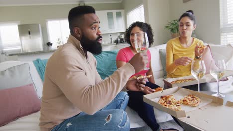 three diverse male and female friends eating pizza and having wine in living room in slow motion