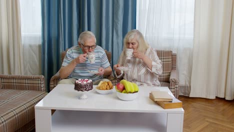 Senior-couple-holding-drinking-tea-talking,-laughing,-smiling,-kissing,-sitting-on-sofa-at-home