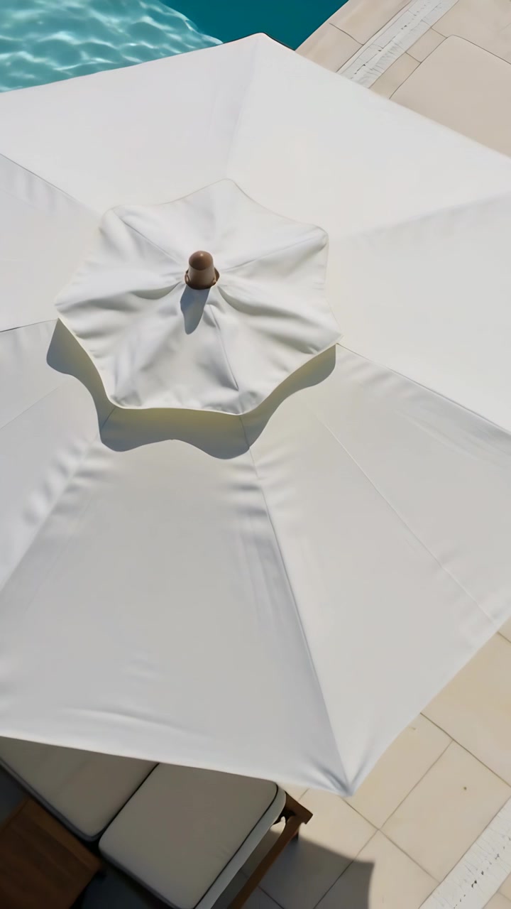 Vertical video: Zooming out camera showing white patio umbrella with brown finial by turquoise pool