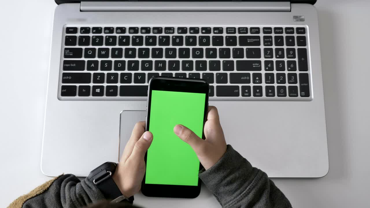 Children's hands use a smartphone, Green screen, chromakey concept, laptop in the background. Top shot 60 fps
