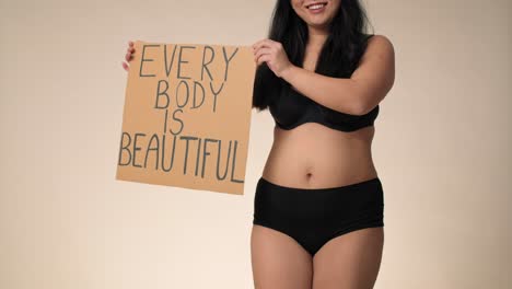 unrecognizable plus size woman in black underwear dancing in the studio and holding a banner.