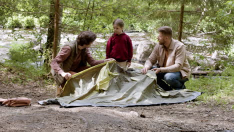 young family setting up tent near the river