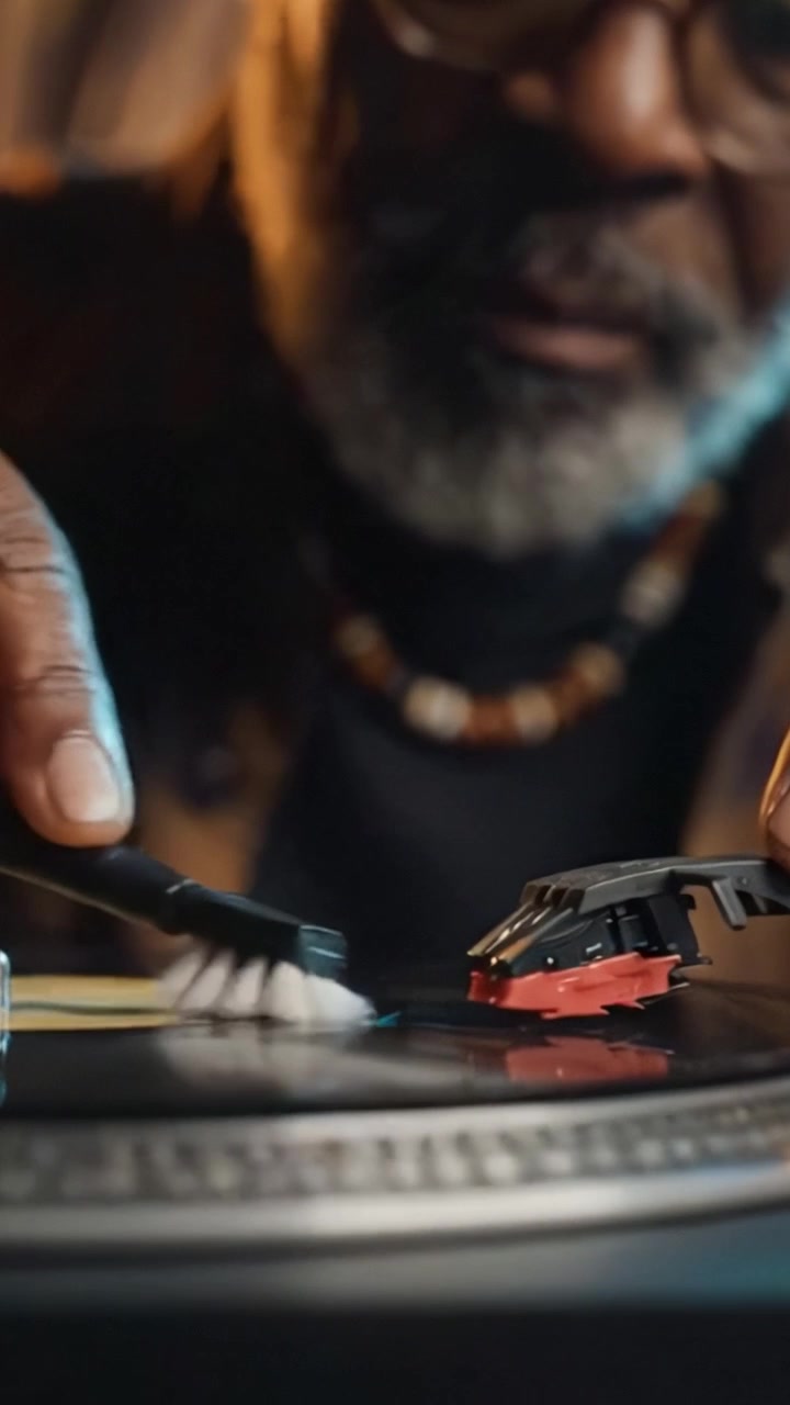 Un DJ esperto crea meticolosamente un'esperienza sonora unica usando un giradischi, mettendo in mostra una passione per la musica con determinazione focalizzata e tecnica esperta.