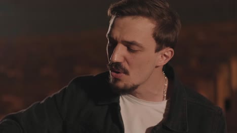 un chico guapo toca una guitarra acústica en un cine abandonado. el músico canta una canción y acompaña en la guitarra