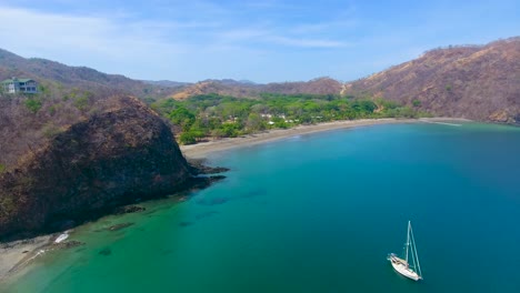 video de dron empujando desde una hermosa playa de arena en costa rica con un solo velero anclado en una bahía de vidrio de agua azul turquesa