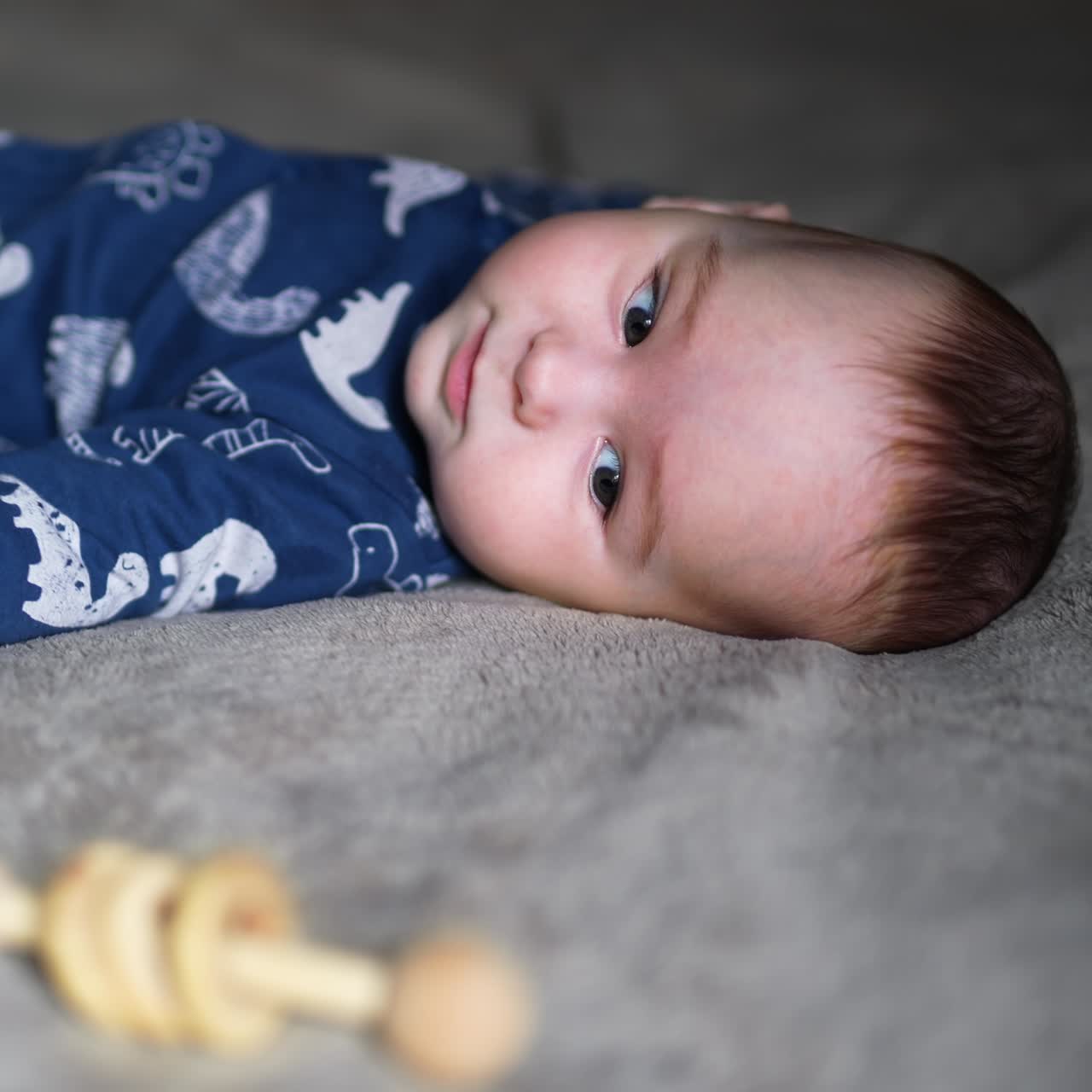 Lovely boy wearing blue clothes lying on his back. Cute baby stretches his hand to a bright toy. Blurred backdrop