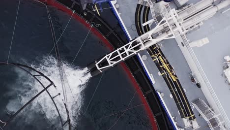 static drone shot of a fish farming vessel flushing fish into a fish pen