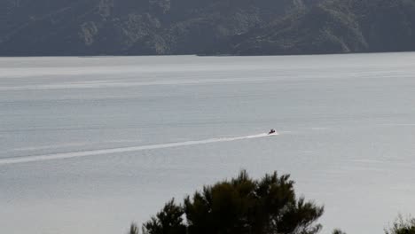 Tiny-speed-boat-driving-through-picturesque,-gigantic-fjords-on-a-sunny-evening-in-New-Zealand