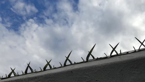 Galvanized-steel-metal-spikes-on-a-property-border-wall-used-for-burglar-proofing-and-security,-sharp-and-dangerous-with-a-beautiful-background-cloud-time-lapse